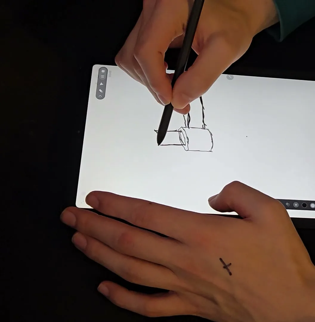 A hand sketching a clamp gripping a cylinder on a drawing tablet.