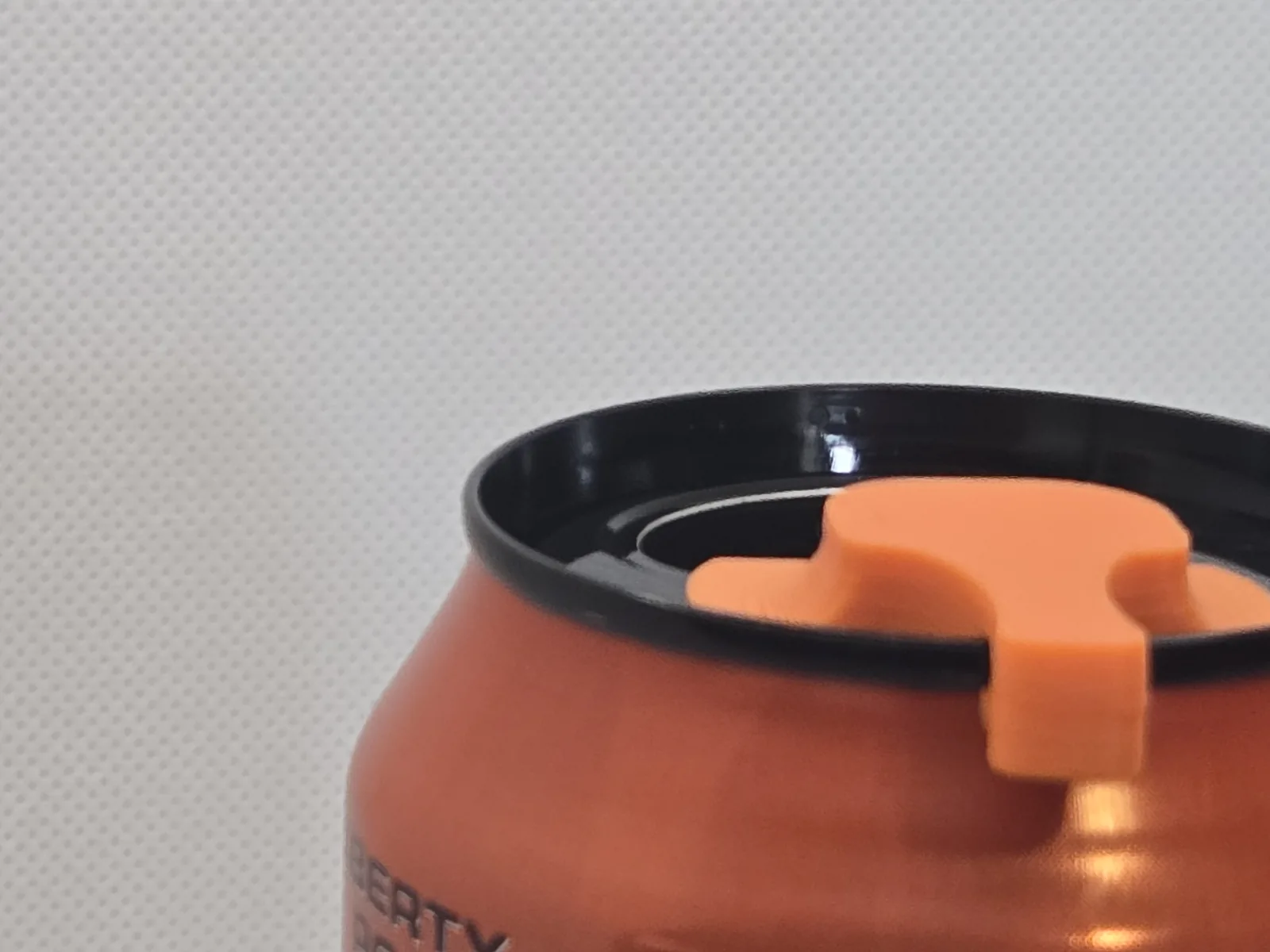 A finger lifting the orange cover, which is seated over the can's pull-tab, cracking the can open.