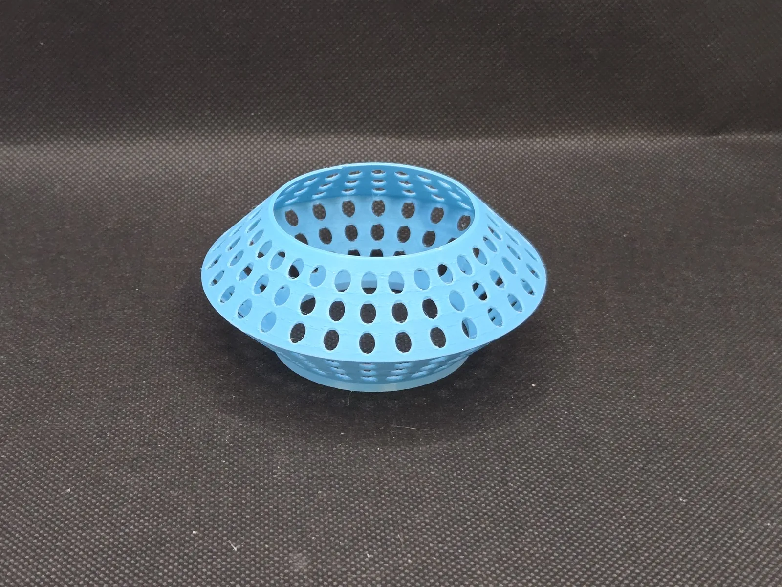 A light blue printed ring, perforated all over with round holes, resting on dark fabric.