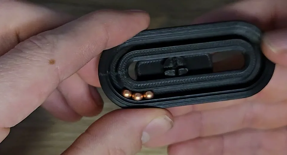 The finished black printed loop held in two hands, with three copper-coloured metal balls visible in the channel.