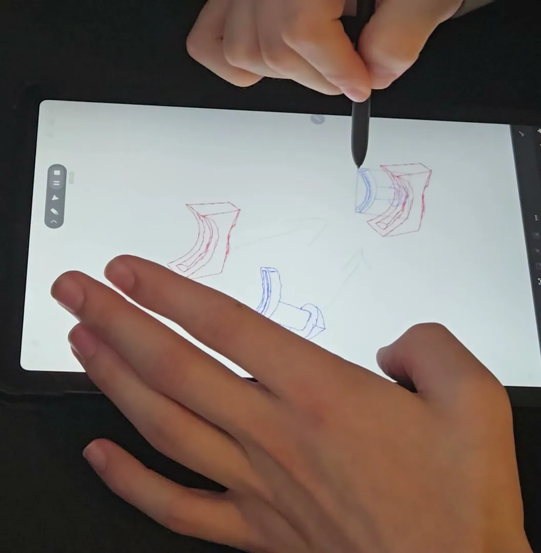 A hand drawing the part on a tablet in red and blue lines, the existing form in one colour and the new geometry in the other.